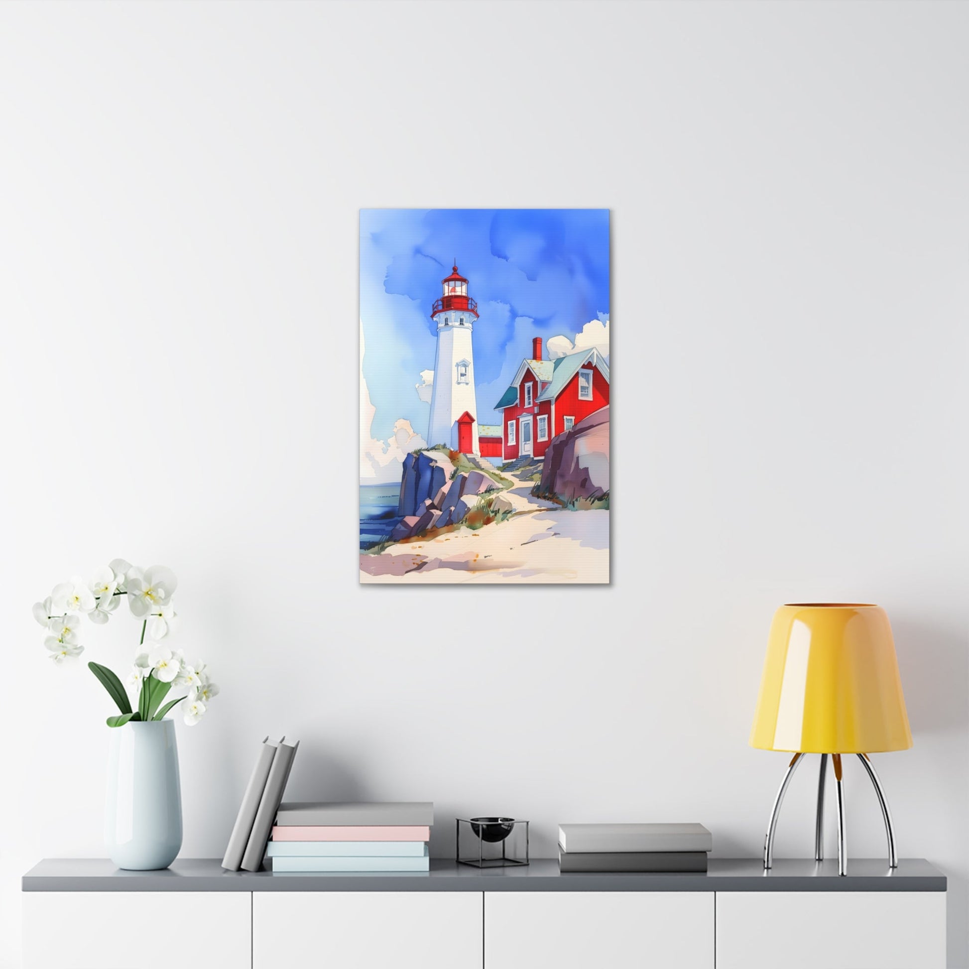 Vertical-oriented wall art: A watercolor-style painting of a lighthouse perched on rocky cliffs overlooking a vast ocean. The sky is painted in shades of blue with wispy white clouds, and the rugged coastline is depicted in intricate detail.